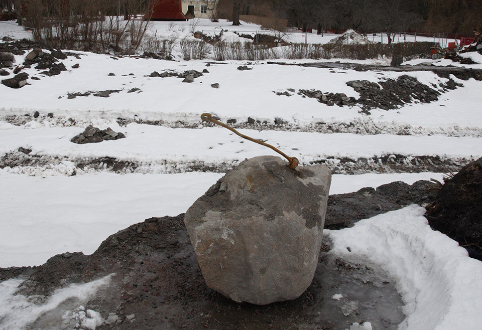 En grå sten med ett fäste bestående av en rostig järnögla och en  rostig järnstång, stenen ligger på ett snöigt område vid centrala gruvområdet
